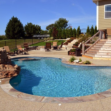 Free form pool with stone table, sun shelf, water feature, and outdoor kitchen,