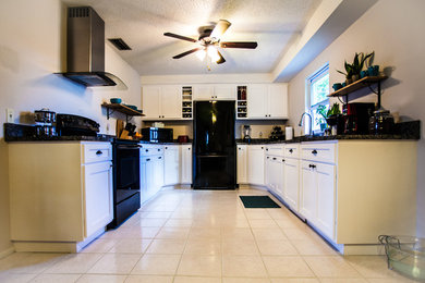This is an example of a large country u-shaped eat-in kitchen in Orlando with an undermount sink, shaker cabinets, white cabinets, granite benchtops, black splashback, stone slab splashback, black appliances, ceramic floors, no island and beige floor.