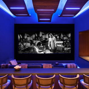 Cette image montre une très grande salle de cinéma design fermée avec un mur bleu, moquette, un écran de projection et un sol multicolore.