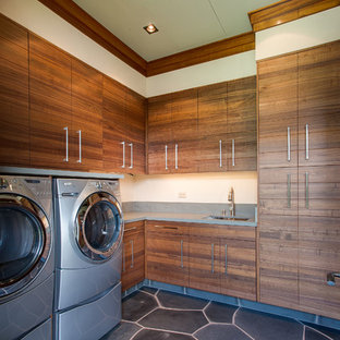 Modelo de lavadero tropical con armarios con paneles lisos, puertas de armario de madera oscura, lavadora y secadora juntas y suelo gris