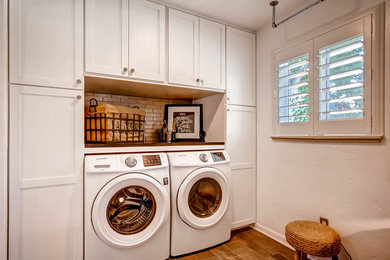 This is an example of a small transitional galley utility room in Denver with shaker cabinets, white cabinets, soapstone benchtops, white walls, ceramic floors and a side-by-side washer and dryer.
