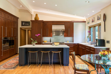 Example of a mid-sized transitional u-shaped light wood floor, brown floor and vaulted ceiling open concept kitchen design in St Louis with an undermount sink, shaker cabinets, brown cabinets, quartz countertops, gray backsplash, glass tile backsplash, paneled appliances, an island and white countertops