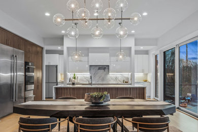 Photo of a large modern l-shaped eat-in kitchen in Detroit with a single-bowl sink, flat-panel cabinets, dark wood cabinets, quartzite benchtops, white splashback, engineered quartz splashback, stainless steel appliances, light hardwood floors, with island, beige floor and white benchtop.