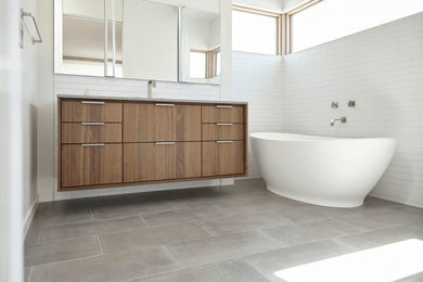 This is an example of a modern bathroom in San Francisco with flat-panel cabinets, medium wood cabinets, a freestanding tub, white tile, subway tile and white walls.