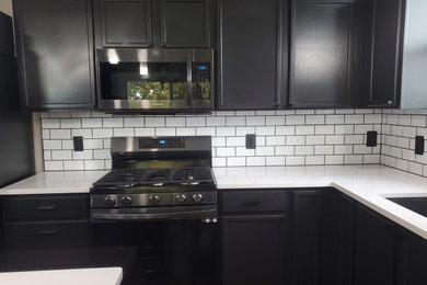 Kitchen pantry - mid-sized modern l-shaped dark wood floor and brown floor kitchen pantry idea in Omaha with an undermount sink, shaker cabinets, black cabinets, white backsplash, subway tile backsplash, stainless steel appliances, an island and white countertops