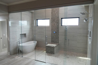 Photo of a large contemporary master bathroom in Chicago with a freestanding tub, a double shower, gray tile, porcelain tile, grey walls, light hardwood floors, grey floor and a sliding shower screen.