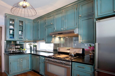 This is an example of a traditional l-shaped separate kitchen in New York with stainless steel appliances, blue cabinets, soapstone benchtops, mirror splashback and beaded inset cabinets.