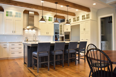 Large transitional u-shaped medium tone wood floor open concept kitchen photo in Other with a farmhouse sink, recessed-panel cabinets, white cabinets, granite countertops, white backsplash, ceramic backsplash, stainless steel appliances and an island