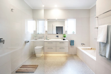 This is an example of a mid-sized modern 3/4 bathroom in Melbourne with flat-panel cabinets, beige cabinets, a drop-in tub, a curbless shower, a one-piece toilet, beige tile, porcelain tile, beige walls, terrazzo floors, a drop-in sink, quartzite benchtops, multi-coloured floor, an open shower and white benchtops.
