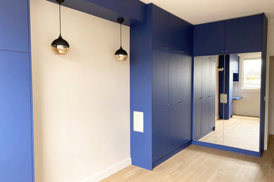 Exemple d'une chambre parentale tendance de taille moyenne avec un mur bleu, parquet clair et dressing.
