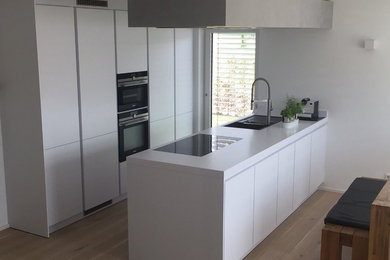 Offene, Zweizeilige, Mittelgroße Moderne Küche mit Doppelwaschbecken, weißen Schränken, Laminat-Arbeitsplatte, Küchengeräten aus Edelstahl, hellem Holzboden und Halbinsel in Stuttgart