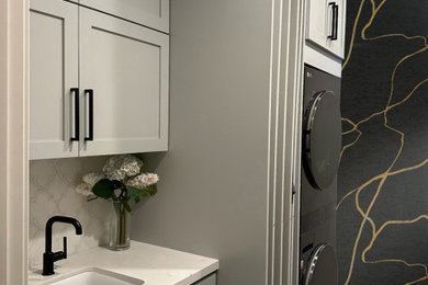 Example of a small trendy single-wall vinyl floor and wallpaper laundry room design in Orange County with an undermount sink, shaker cabinets, gray cabinets, a stacked washer/dryer and white countertops