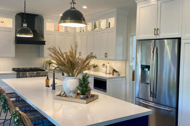 Inspiration for a mid-sized modern medium tone wood floor and brown floor eat-in kitchen remodel in Orange County with a farmhouse sink, shaker cabinets, blue cabinets, quartz countertops, white backsplash, quartz backsplash, black appliances, an island and white countertops