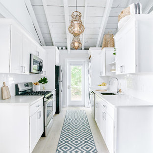 Bild på ett litet maritimt vit vitt kök, med en enkel diskho, luckor med infälld panel, vita skåp, granitbänkskiva, vitt stänkskydd, stänkskydd i keramik, rostfria vitvaror, ljust trägolv och beiget golv