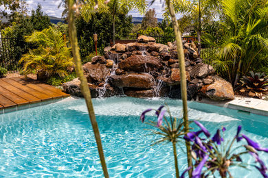 Imagen de piscina natural exótica grande a medida en patio trasero con paisajismo de piscina y adoquines de piedra natural