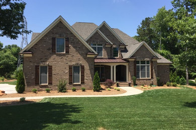 Large transitional brown two-story brick exterior home photo in Charlotte with a shingle roof