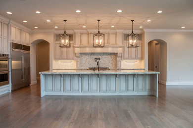 Example of a large transitional l-shaped medium tone wood floor kitchen design in Other with granite countertops, beige backsplash, stainless steel appliances, an undermount sink, raised-panel cabinets, beige cabinets, mosaic tile backsplash and an island