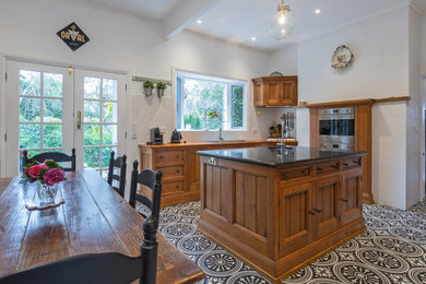 Country kitchen in Melbourne with granite benchtops, stainless steel appliances, porcelain floors, black benchtop and recessed-panel cabinets.
