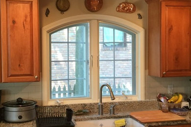 Example of a farmhouse kitchen design in Detroit with a farmhouse sink, light wood cabinets, granite countertops, beige backsplash, cement tile backsplash and stainless steel appliances