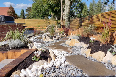 This is an example of a medium sized contemporary back formal full sun garden for summer in Dorset with a retaining wall, decorative stones and a wood fence.