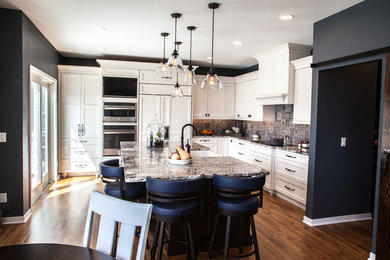 Example of a large transitional u-shaped light wood floor and brown floor open concept kitchen design in Other with a farmhouse sink, shaker cabinets, white cabinets, granite countertops, gray backsplash, mosaic tile backsplash, paneled appliances and an island