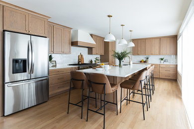 Example of a large transitional l-shaped light wood floor open concept kitchen design in Chicago with an undermount sink, recessed-panel cabinets, medium tone wood cabinets, quartz countertops, white backsplash, marble backsplash, stainless steel appliances, an island and white countertops