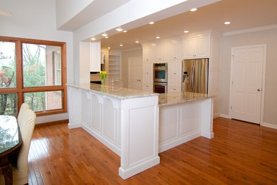 Example of a mid-sized classic u-shaped light wood floor eat-in kitchen design in Other with a farmhouse sink, raised-panel cabinets, white cabinets, granite countertops, white backsplash, subway tile backsplash, stainless steel appliances and a peninsula
