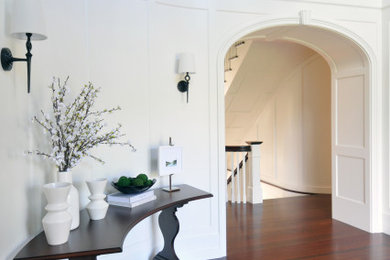This is an example of a large beach style foyer in Boston with white walls, dark hardwood floors and panelled walls.
