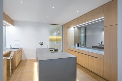 Moderne Wohnküche mit Kücheninsel, integriertem Waschbecken, flächenbündigen Schrankfronten, Edelstahl-Arbeitsplatte, Rückwand aus Spiegelfliesen und hellem Holzboden in München