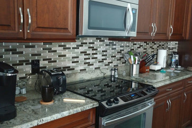 Inspiration for a large timeless single-wall porcelain tile and gray floor enclosed kitchen remodel in Tampa with an undermount sink, raised-panel cabinets, medium tone wood cabinets, granite countertops, multicolored backsplash, glass tile backsplash, stainless steel appliances, multicolored countertops and an island