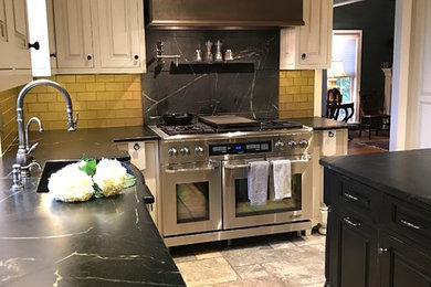 Eat-in kitchen - traditional l-shaped travertine floor eat-in kitchen idea in Philadelphia with a farmhouse sink, beaded inset cabinets, white cabinets, soapstone countertops, yellow backsplash, glass tile backsplash, paneled appliances and an island
