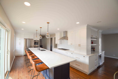 This is an example of a large transitional eat-in kitchen in Chicago with white cabinets, quartz benchtops, white splashback, stainless steel appliances, medium hardwood floors, with island and white benchtop.