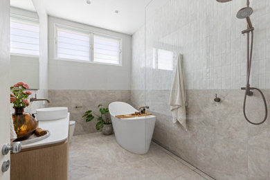 Large contemporary bathroom in Sydney with flat-panel cabinets, light wood cabinets, a freestanding tub, an open shower, a one-piece toilet, beige tile, beige walls, a vessel sink, grey floor, an open shower, white benchtops, a niche, a single vanity and a floating vanity.