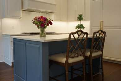 Example of a mid-sized classic u-shaped dark wood floor and brown floor enclosed kitchen design in Austin with raised-panel cabinets, white cabinets, quartzite countertops, white backsplash, ceramic backsplash, stainless steel appliances, an island and white countertops