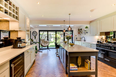 This is an example of a large contemporary grey and white open plan kitchen in Sussex with a built-in sink, shaker cabinets, grey cabinets, quartz worktops, metallic splashback, glass sheet splashback, black appliances, vinyl flooring, an island, brown floors, white worktops and feature lighting.