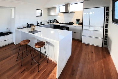 Photo of a mid-sized beach style u-shaped open plan kitchen in Perth with an undermount sink, quartz benchtops, white splashback, ceramic splashback, light hardwood floors, brown floor, white benchtop and vaulted.