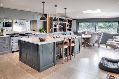 Large contemporary l-shaped kitchen/diner in Other with a belfast sink, flat-panel cabinets, grey cabinets, quartz worktops, metallic splashback, mirror splashback, stainless steel appliances, limestone flooring, an island, beige floors and white worktops.