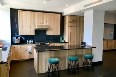 Mid-sized trendy l-shaped black floor eat-in kitchen photo in New York with an undermount sink, flat-panel cabinets, medium tone wood cabinets, marble countertops, black backsplash, marble backsplash, paneled appliances, an island and black countertops