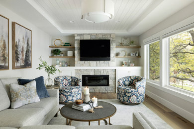 Example of a mid-sized beach style formal and loft-style light wood floor, brown floor and tray ceiling living room design in Minneapolis with gray walls, a standard fireplace, a stone fireplace and a wall-mounted tv