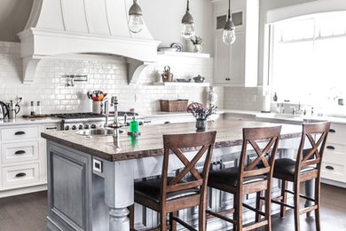 Example of a mid-sized mountain style l-shaped medium tone wood floor and brown floor eat-in kitchen design in Vancouver with a farmhouse sink, shaker cabinets, white cabinets, quartzite countertops, white backsplash, subway tile backsplash, stainless steel appliances and an island