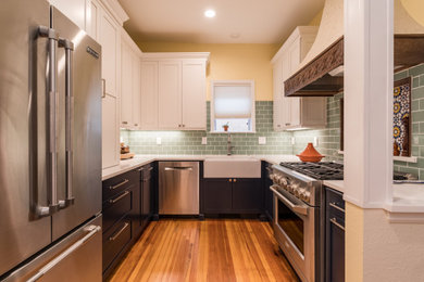 Photo of a mid-sized arts and crafts u-shaped eat-in kitchen in Denver with a farmhouse sink, shaker cabinets, white cabinets, quartz benchtops, multi-coloured splashback, glass tile splashback, stainless steel appliances, medium hardwood floors, a peninsula, brown floor and white benchtop.