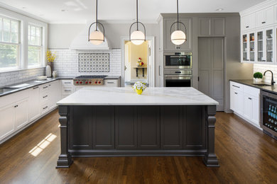 This is an example of a classic u-shaped kitchen pantry in Minneapolis with recessed-panel cabinets, grey cabinets, engineered stone countertops, white splashback, ceramic splashback, stainless steel appliances, dark hardwood flooring, an island and grey worktops.