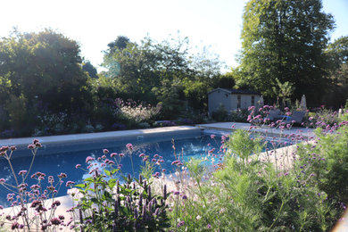 Diseño de piscina clásica grande en patio trasero con paisajismo de piscina y adoquines de piedra natural