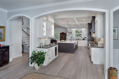 Example of a large transitional light wood floor and brown floor kitchen design in Miami with glass-front cabinets, white cabinets, white backsplash, marble backsplash, paneled appliances, an island, a farmhouse sink and marble countertops
