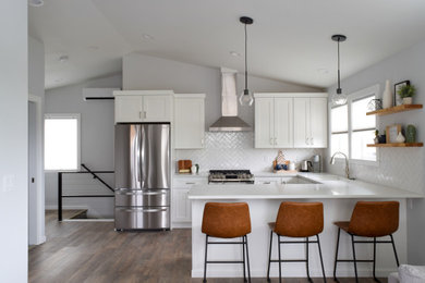 Kitchen - contemporary u-shaped vinyl floor kitchen idea in Seattle with an undermount sink, shaker cabinets, white cabinets, solid surface countertops, white backsplash, porcelain backsplash, stainless steel appliances and white countertops
