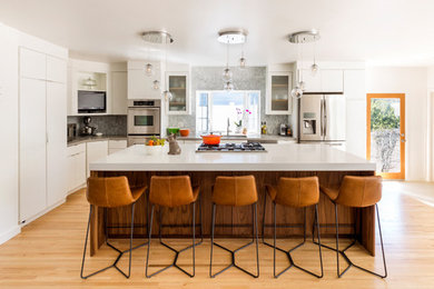 Mid-sized 1950s l-shaped light wood floor kitchen photo in Los Angeles with a drop-in sink, flat-panel cabinets, white cabinets, quartzite countertops, gray backsplash, marble backsplash, stainless steel appliances and an island
