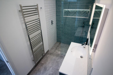 Small contemporary ensuite half tiled bathroom in Gloucestershire with shaker cabinets, blue cabinets, a walk-in shower, a wall mounted toilet, blue tiles, ceramic tiles, white walls, porcelain flooring, a built-in sink, grey floors, an open shower, white worktops, feature lighting, a single sink and a built in vanity unit.