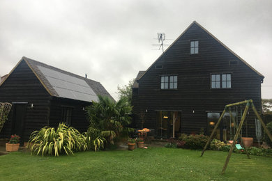 Cette image montre une façade de maison noire minimaliste en bois et planches et couvre-joints de plain-pied avec un toit à deux pans, un toit en tuile et un toit marron.