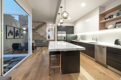 Medium sized contemporary galley open plan kitchen in Gold Coast - Tweed with a built-in sink, flat-panel cabinets, black cabinets, granite worktops, stainless steel appliances, light hardwood flooring, an island and white worktops.