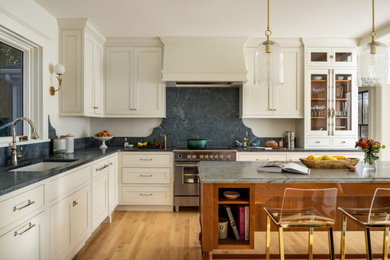 Example of a mid-sized classic l-shaped medium tone wood floor and brown floor kitchen design in Boston with an undermount sink, white cabinets, soapstone countertops, stone slab backsplash, stainless steel appliances, an island, recessed-panel cabinets, gray backsplash and gray countertops